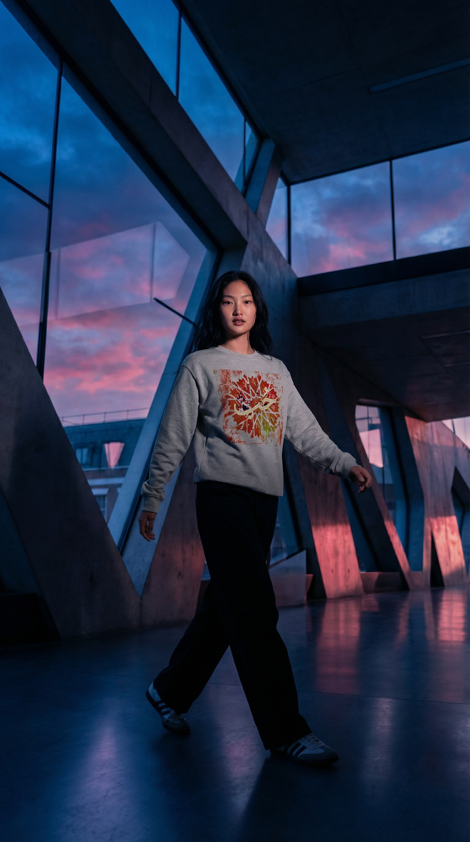 Person wearing a MOEBEER light gray sweatshirt with a colorful design, standing in a futuristic indoor setting with a pink and purple sky.